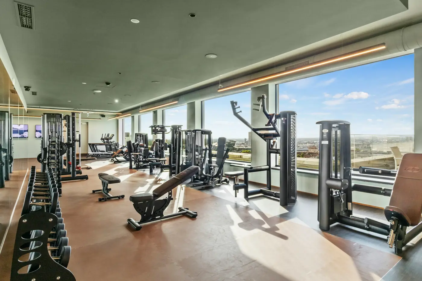 A bright gym floor with strength machines by a wall of windows